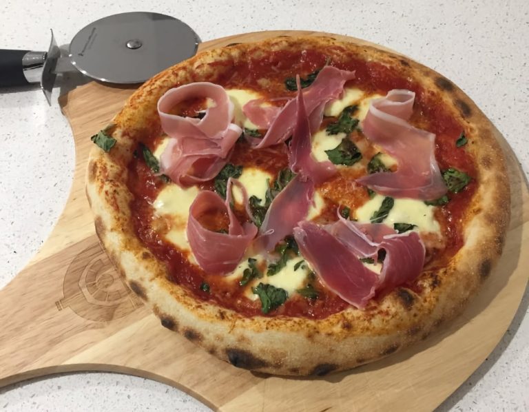 Freshly baked pizza featuring ham and cheese, elegantly displayed on a wooden board.